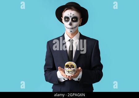 Junger Mann mit gemaltem Gesicht und Zuckerschädel für Mexikos Tag der Toten (El Dia de Muertos) auf farbigem Hintergrund Stockfoto