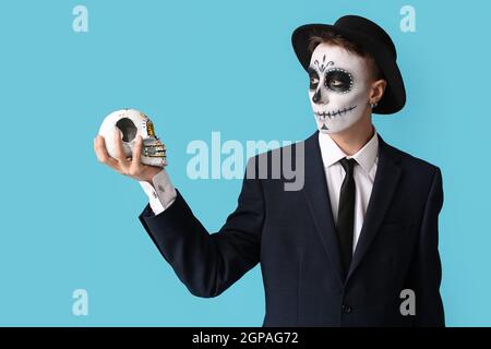 Junger Mann mit gemaltem Gesicht und Zuckerschädel für Mexikos Tag der Toten (El Dia de Muertos) auf farbigem Hintergrund Stockfoto