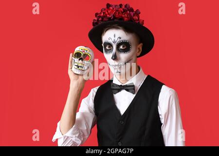 Junger Mann mit gemaltem Gesicht und Zuckerschädel für Mexikos Tag der Toten (El Dia de Muertos) auf farbigem Hintergrund Stockfoto