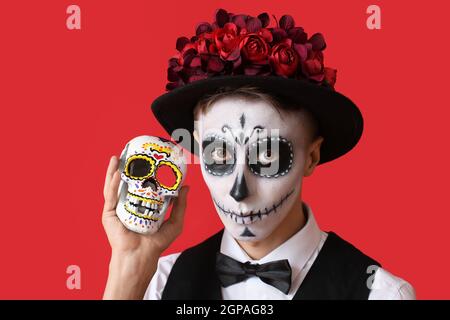 Junger Mann mit gemaltem Gesicht und Zuckerschädel für Mexikos Tag der Toten (El Dia de Muertos) auf farbigem Hintergrund Stockfoto