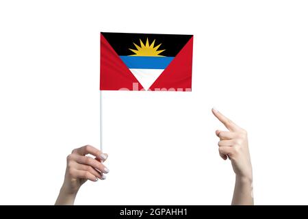 Eine schöne weibliche Hand hält eine Antigua und Barbuda Flagge, auf die sie den Finger ihrer anderen Hand zeigt, isoliert auf weißem Hintergrund. Stockfoto