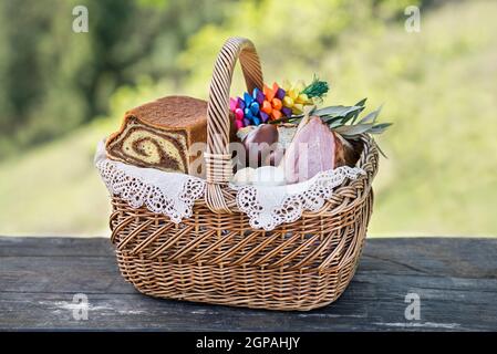 Ostern traditionelle Küche mit Schinken, Eiern und Brot im Korb. Urlaub im Freien. Osterkorb mit allerlei köstlichen Delikatessen gefüllt Stockfoto