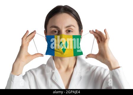 Atemschutzmaske mit Flagge von St. Vincent und die Grenadinen Arzt setzt auf medizinische Gesichtsmaske isoliert auf weißem Hintergrund. Stockfoto