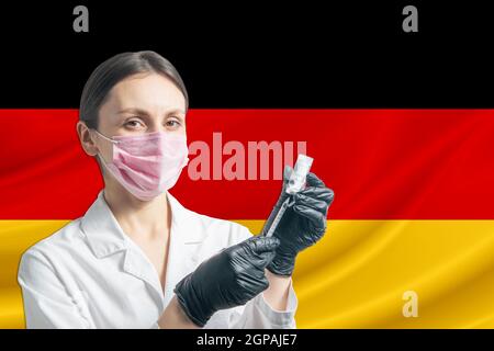 Ärztin bereitet die Impfung vor dem Hintergrund der deutschen Flagge vor. Impfkonzept Deutschland. Stockfoto