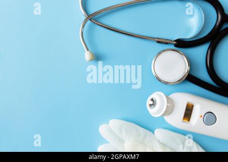 Behandlungskonzept der Medizin. Elektronisches Thermometer, Phonendoskop oder Stethoskop, weiße Handschuhe auf blauem Hintergrund. Hochwertige Fotos Stockfoto