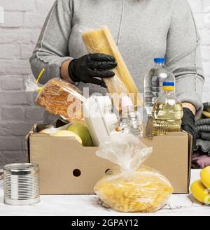 Frau in einem grauen Pullover verpackt Lebensmittel in einem Karton, das Konzept der Hilfe und Freiwilligenarbeit, Spende Stockfoto