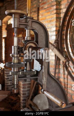 Veraltete Stahlbohrmaschine mit offenem Getriebe und manueller Bedienung in einer restaurierten Schmiede. Stockfoto