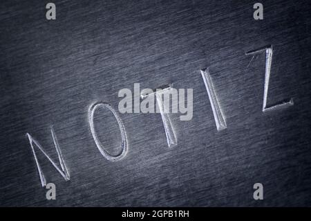 Nahaufnahme einer grauen abgeschrägten Metallplatte mit dem Wort NOTE diagonal eingestanzt. Stockfoto