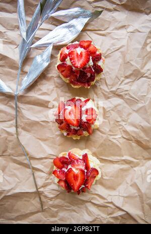 Schöne kleine Kuchen mit Erdbeeren zusammen mit einem Zweig auf Kraftpapier. Stockfoto