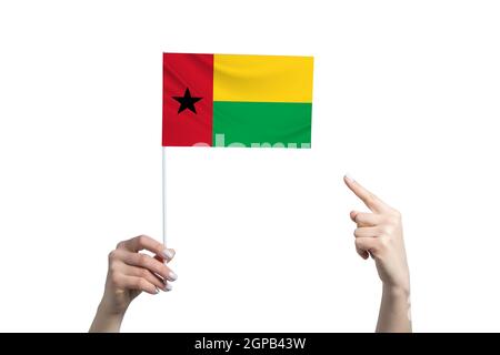 Eine schöne weibliche Hand hält eine Guinea-Bissau-Fahne, zu der sie den Finger ihrer anderen Hand zeigt, isoliert auf weißem Hintergrund. Stockfoto