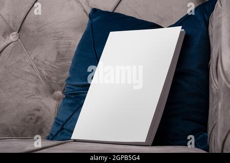 Buch mit leerem Bezug auf Samt Sofa blaues Kissen, editierbare Mock-up-Serie bereit für Ihr Design, Abdeckung Auswahlpfad enthalten. Stockfoto