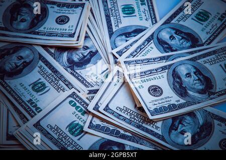 Bargeld von hundert Dollar Scheinen, Dollar Hintergrundbild. Hundert US-Banknoten sind über den Hintergrund verstreut. Blaue Farbe und Vignettierung. Stockfoto