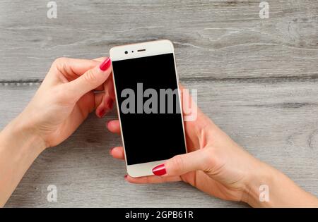 Ansicht von oben auf die junge Frau Hände, mit roten Nägeln, Holding weißen Smart Phone. Schwarzer Bildschirm wählen Sie Ihr Bild oder Text hinzufügen. Stockfoto