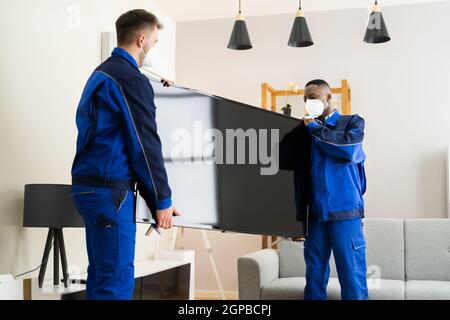 Zwei junge männliche Movers in Uniform, Fernseher im Wohnzimmer Stockfoto