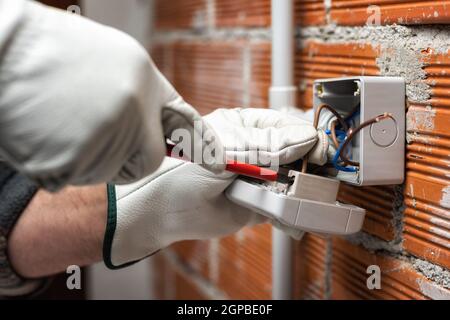 Elektriker Arbeiter bei der Arbeit mit Schraubendreher fixiert das Kabel in den Buchsen eines Wohnelektrik-System. Bauindustrie. Stockfoto