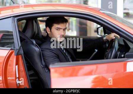 Der junge Geschäftsmann in einem schwarzen Anzug öffnet die Tür des Sportwagens, während er das Rad hält. Stockfoto