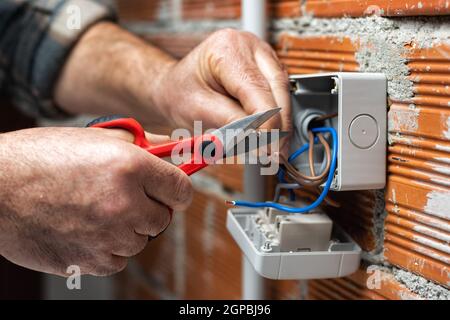 Der Elektriker Arbeiter bei der Arbeit mit der Schere bereitet die elektrischen Kabel des häuslichen elektrischen Systems vor. Bauindustrie. Stockfoto