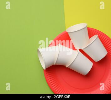 Stapel weißer Pappbecher und roter runder Teller auf grünem Hintergrund. Kunststoffabstoßungskonzept, keine Verschwendung Stockfoto