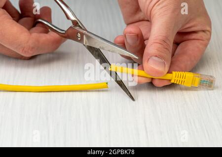 Internet zensieren Schneiden ein gelbes Netzwerkkabel mit Schere. Eingeschränkter Internetzugang Konzept Stockfoto