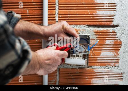 Der Elektriker Arbeiter bei der Arbeit mit der Schere bereitet die elektrischen Kabel des häuslichen elektrischen Systems vor. Bauindustrie. Stockfoto