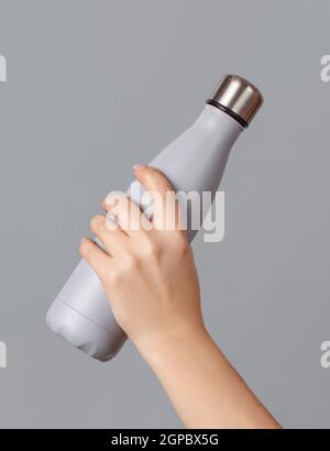 Hand mit grauer wiederverwendbarer Isolierflasche auf grauem Hintergrund. Zero Waste, plastikfreies und nachhaltiges Lifestyle-Konzept Stockfoto