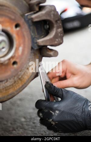 Nahaufnahme eines Mechanikers, der an einem abgenutzten und rostigen Auto arbeitet, Bremsscheibe und Bremssattel. Stockfoto