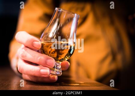Farbe Nahaufnahme eine Hand hält ein Glencairn Whisky Glas auf einem Holztisch, mit geringer Schärfentiefe. Stockfoto