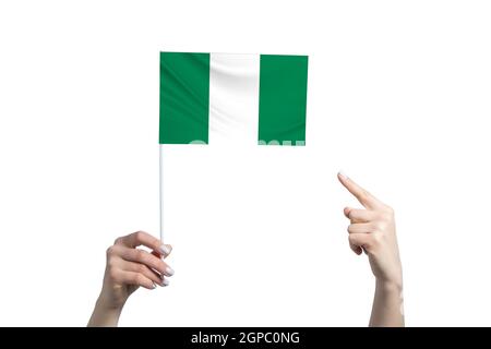 Eine schöne weibliche Hand hält eine Nigeria-Flagge, auf der sie den Finger ihrer anderen Hand zeigt, isoliert auf weißem Hintergrund. Stockfoto