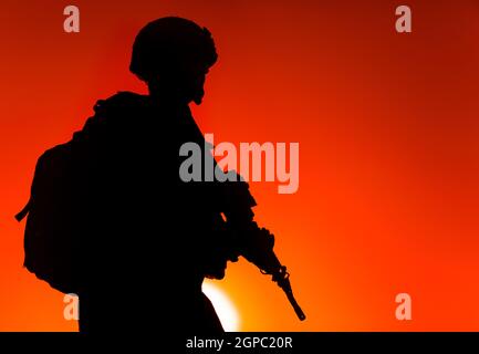 Silhouette des Armeekrieges in Helm und Munitionsform, mit taktischem Rucksack, mit Dienstgewehr auf dem Hintergrund des Sonnenuntergangs. Zählerstand Stockfoto