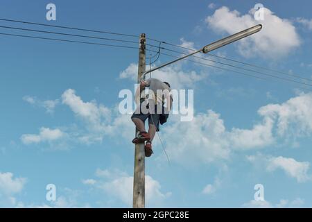 Elektriker, Mechaniker klettern und arbeiten an elektrischen Masten. Konzept der falschen Arbeitsweise und keine Sicherheit kein Helm. Stockfoto