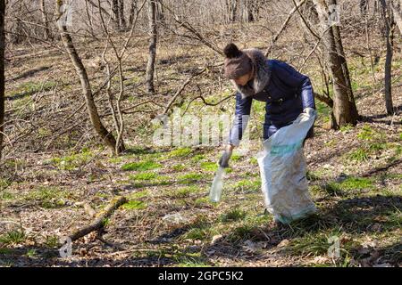 Das Mädchen sammelt Müll im Wald, nimmt eine Plastikflasche und legt sie in eine Tasche Stockfoto