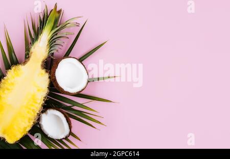 Flach legen mit geschnittenen Hälften aus frischer Ananas, Kokosnuss und grünem Palmblatt auf pastellrosa Hintergrund. Zutat für Pina Colada. Exotische Früchte. Hohes q Stockfoto