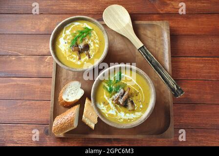 Kürbiscremesuppe mit Sahne und Pilzen in zwei Holzschäften Schüsseln auf Holzhintergrund Stockfoto