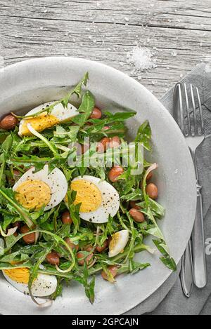 Frischer Löwenzahn-Salat mit Bohnen und Eiern auf Holzhintergrund Stockfoto