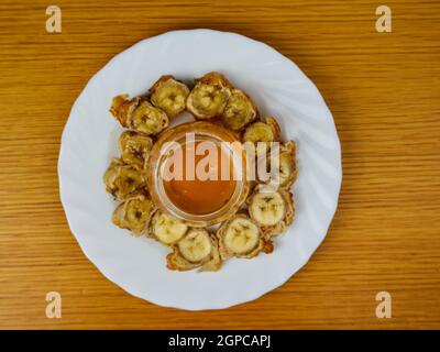 Gebratene Scheiben des reifen Kochbananen und ein Glas Honig, der einen Bienenstock auf einem runden Holzteller herstellt. Draufsicht Stockfoto