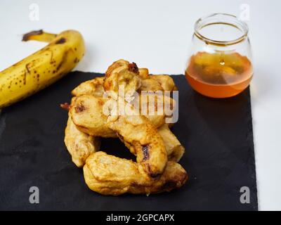 Gebratene Scheiben der reifen Kochbanane mit einer Banane verziert Und Honig auf einem schwarzen Schieferbrett Stockfoto