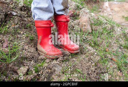 Kleiner Junge trägt rote schlammige Regenstiefel. Regenzeit und Kinderkonzept Stockfoto