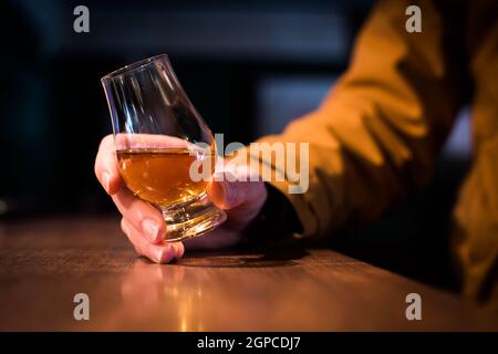 Farbe Nahaufnahme eine Hand hält ein Glencairn Whisky Glas auf einem Holztisch, mit geringer Schärfentiefe. Stockfoto