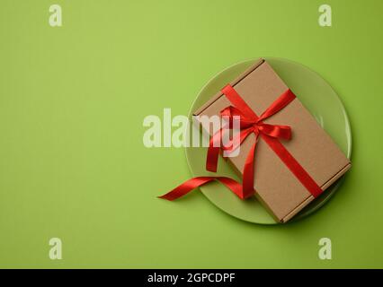Rechteckiger brauner Karton mit einem roten Band gebunden und liegt auf einer grünen Keramik, Draufsicht, Kopierraum Stockfoto
