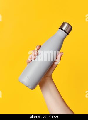 Hand mit grauer wiederverwendbarer Isolierflasche auf gelbem Hintergrund. Zero Waste, plastikfreies und nachhaltiges Lifestyle-Konzept Stockfoto