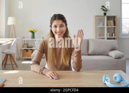 Die junge Bloggerin winkt mit der Hand, während sie Videos aufnimmt oder zu Hause online anruft. Stockfoto