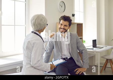 Glücklicher junger Mann, der während der Konsultation in einer modernen Klinik oder einem Krankenhaus dem Arzt zuhört Stockfoto