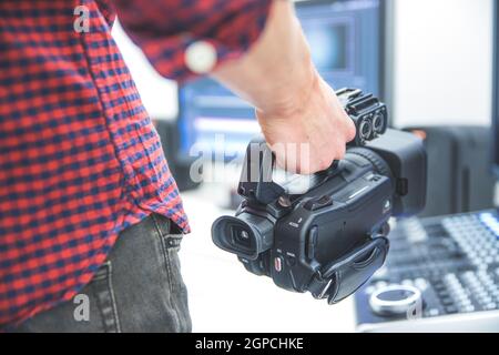 Der männliche Kameramann hält einen professionellen Camcorder mit unscharfem Hintergrund Stockfoto