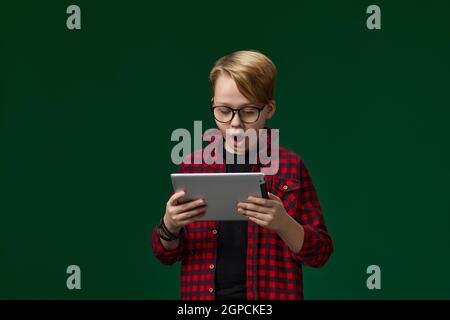 Überrascht kaukasischen Kind Junge in einer Brille mit digitalen Tablet auf Grüner Hintergrund Stockfoto