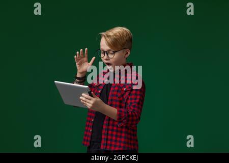 Super aufgeregt Kind Junge in Brille mit digitalen Tablet auf Grüner Hintergrund Stockfoto