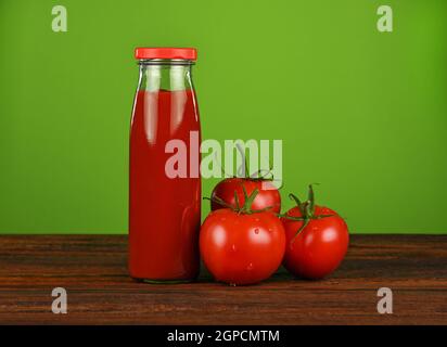 Nahaufnahme eine Glasflasche Ketchup-Sauce und frische rote Tomaten auf Holztisch auf grünem Hintergrund mit Kopierraum, Low-Angle-Ansicht Stockfoto