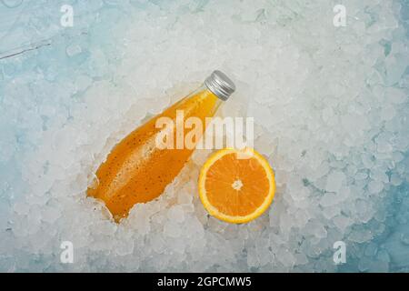 Nahaufnahme eine Glasflasche mit kaltem Orangensaft Cocktail-Drink mit Chiasamen und halb geschnittener Orange auf zerkleinertem Eis im Einzelhandel, hoher Angl Stockfoto