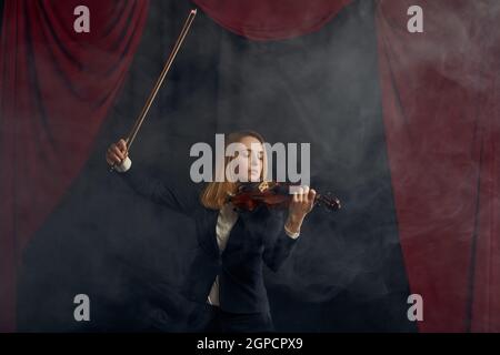 Violinistin mit Bogen und Violine, Solokonzert auf der Bühne. Frau mit Streichmusikinstrument, Musikkunst, Musikerspiel auf Viola, dunkler Hintergrund Stockfoto