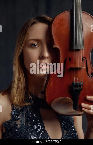 Violinistin mit Retro-Geige im Gesicht. Frau mit Streichmusikinstrument, Musikkunst, Musikerspiel auf Viola, dunkler Hintergrund Stockfoto