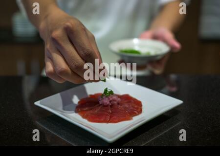 Der Küchenchef bereitet Thunfisch-Sashimi zu. Der Prozess der Herstellung und Dekoration Thunfisch Sashimi. Thunfisch-Sashimi auf weißem Teller. Traditionelles japanisches Essen. Stockfoto